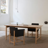Natural wood table with smooth finish, complemented by black leather chairs and soft beige rug. Minimalist design.