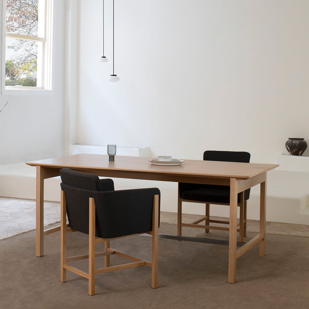 Light wood dining table with black upholstered chairs in a minimalist setting. Neutral tones enhance modern decor.