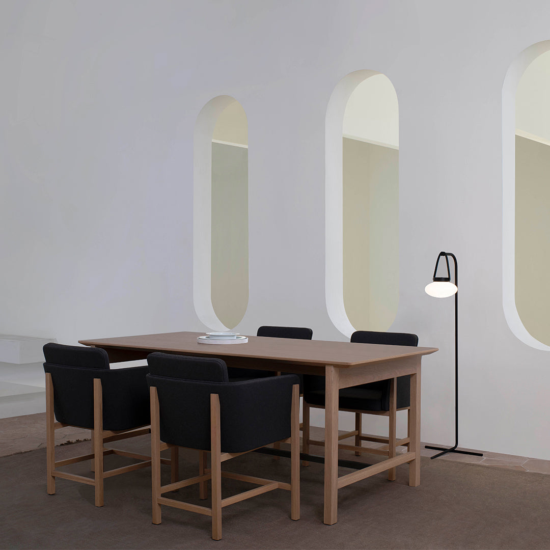 Modern wooden dining table with black upholstered chairs, set against a neutral-toned, minimalist interior.