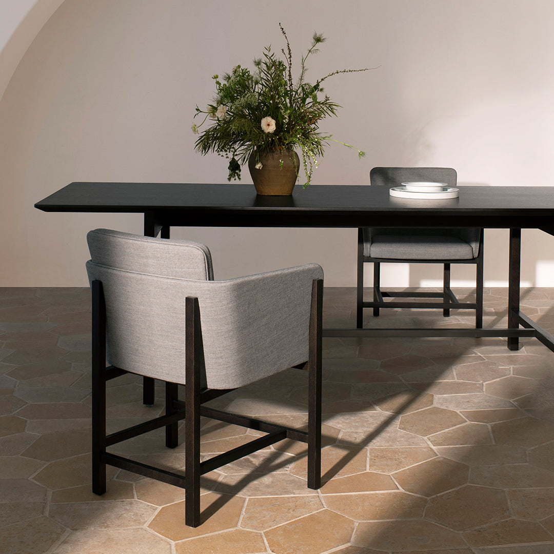 Light gray upholstered chair with a sleek black frame, set against a warm, honey-toned stone floor.