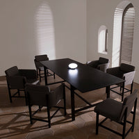 Modern black dining table with gray upholstered chairs, featuring soft light and shadow patterns on a neutral floor.