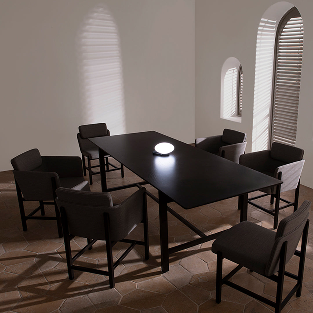 Modern black dining table with gray upholstered chairs, featuring a minimalist design and subtle shadow patterns on the walls.