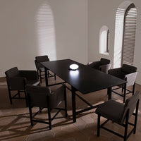 Modern black dining table with gray upholstered chairs, featuring a minimalist design and subtle shadow patterns on the walls.