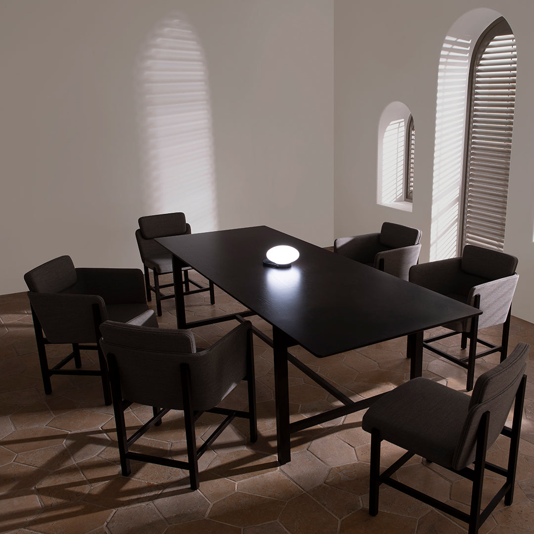 Modern black dining table with minimalist design, paired with gray upholstered chairs in a softly lit, neutral-toned room.
