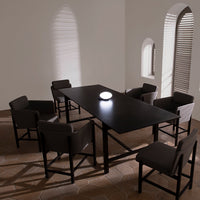 Modern black dining table with minimalist design, paired with gray upholstered chairs in a softly lit, neutral-toned room.