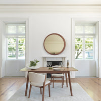 Modern dining room featuring a round wooden mirror, neutral beige chairs, and a light wood table on a soft gray rug.