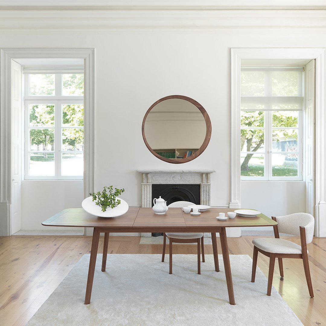 Modern wooden dining table with a warm brown finish, surrounded by neutral-colored chairs and a soft, light rug.