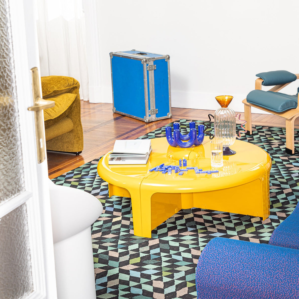 Vibrant yellow coffee table on a patterned black and green geometric rug with blue accents and colorful decor elements.