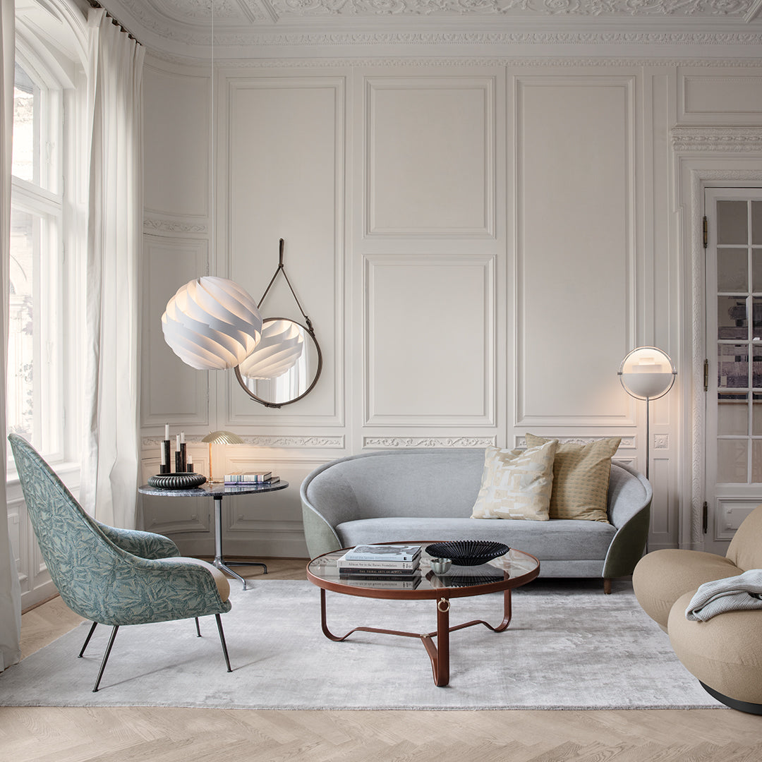Light gray sofa with green accent chair, soft beige and cream pillows, and a textured white area rug in a modern room.