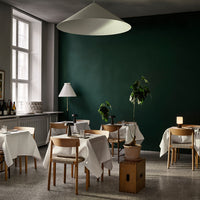 Neutral-toned furniture with white tablecloths against a dark green wall, featuring a light gray floor and potted plant accents.