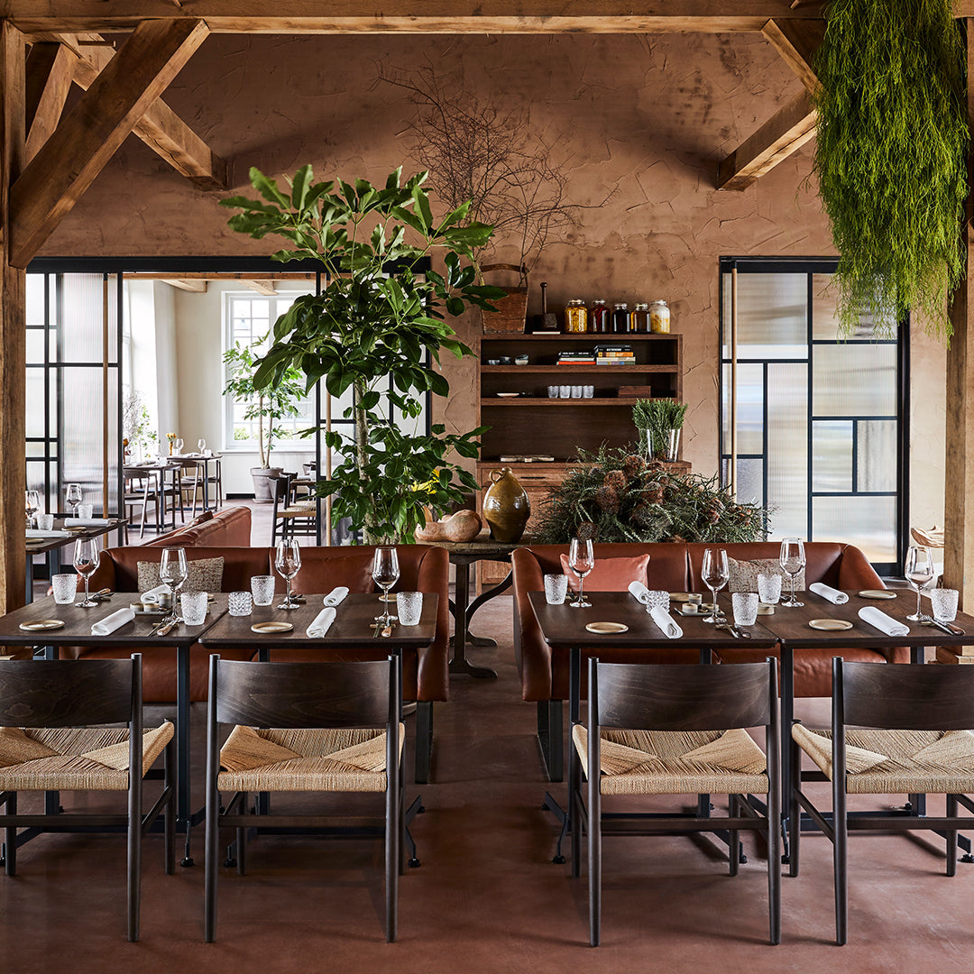 Warm earthy tones with wooden furniture, woven seating, and lush greenery create a cozy dining atmosphere.