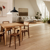 "Light wooden dining set with natural tones and contrasting dark chairs in a modern, airy interior."