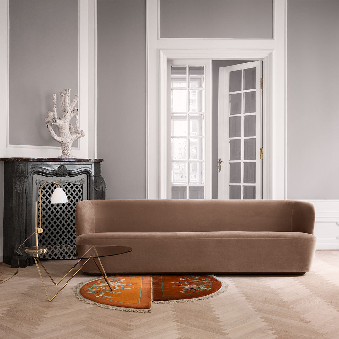 Brown velvet sofa against a gray wall, paired with an orange patterned rug and gold-accented side table.