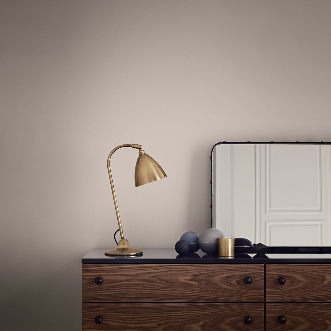 Gold lamp on wooden dresser against a soft beige wall, featuring sleek lines and simple geometric patterns.