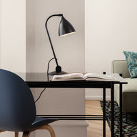 Modern black desk lamp on a sleek black table, with a solid blue chair and a patterned rug in muted tones.