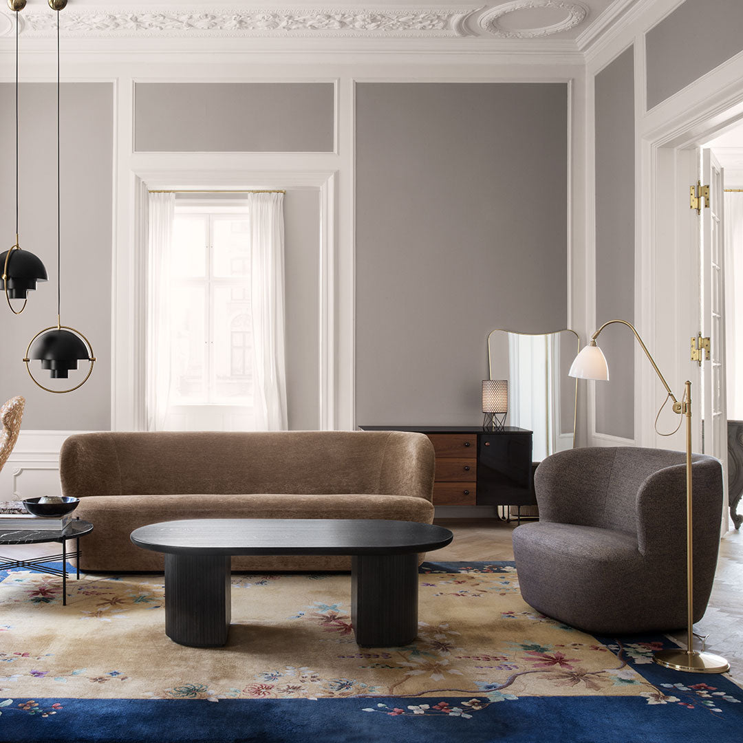 Stylish living room with neutral beige sofa, dark gray armchair, black coffee table, and a colorful blue-patterned rug.