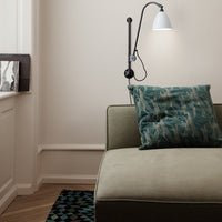 Teal abstract pillow on an olive green couch, paired with a geometric patterned rug in deep blue and green hues.