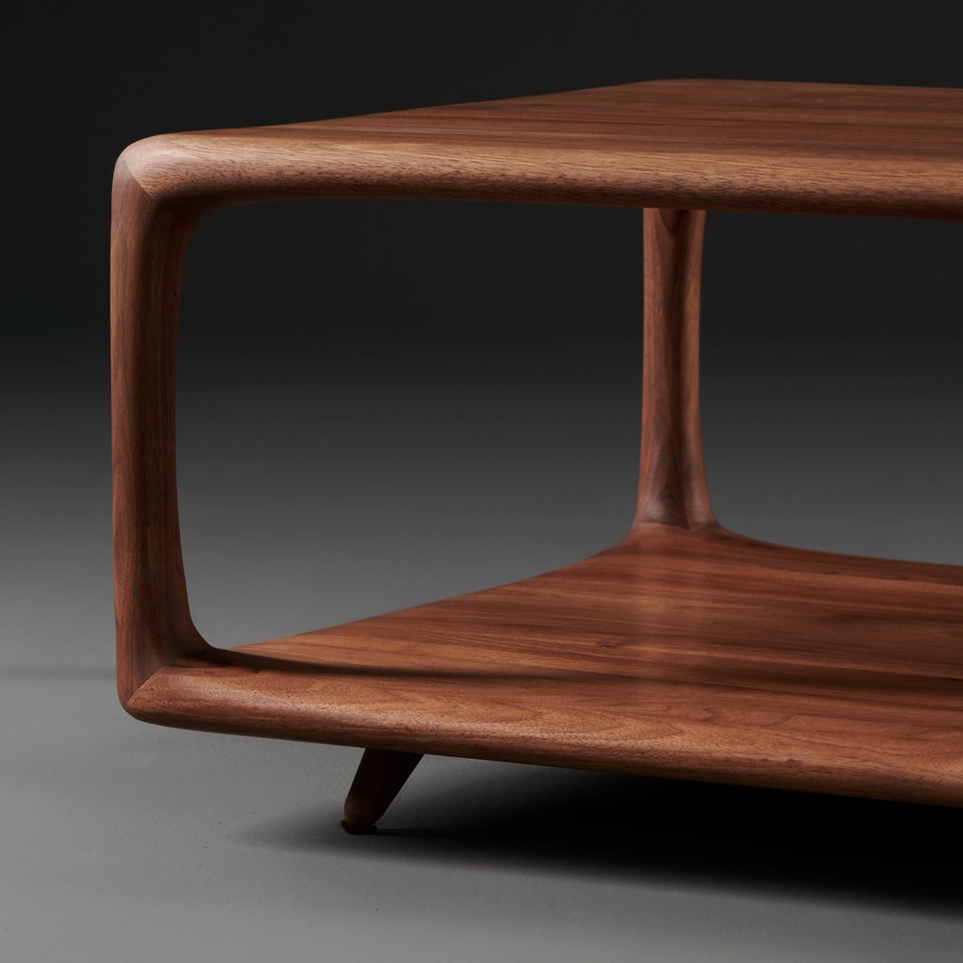 Walnut wood coffee table with smooth, curved edges and rich, warm brown tones. Minimalist design with open shelving.