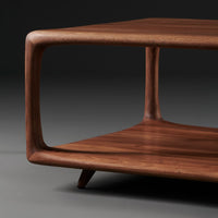 Walnut wood coffee table with smooth, curved edges and rich, warm brown tones. Minimalist design with open shelving.