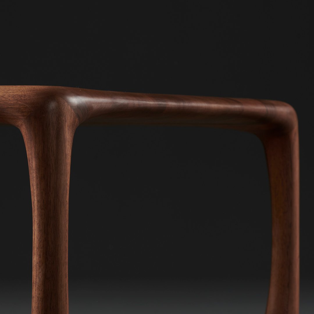 Brown wood table leg with smooth curves against a dark background, highlighting natural grain patterns.