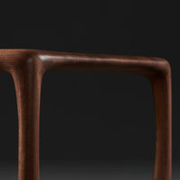 Brown wood table leg with smooth curves against a dark background, highlighting natural grain patterns.