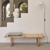 Natural wood bench with a woven pattern, featuring a gray blanket for added texture and warmth.