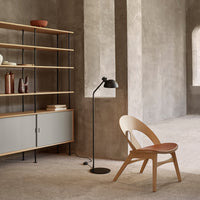 Minimalist beige and gray interior with wooden shelving, black lamp, and a light wood chair with a terracotta seat.