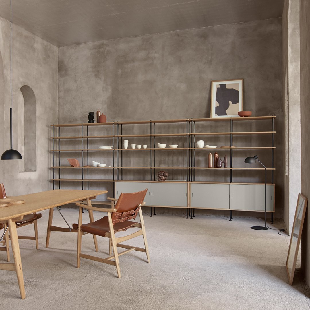 Modern wooden shelving unit with black metal accents, set against a textured gray wall and beige carpet.
