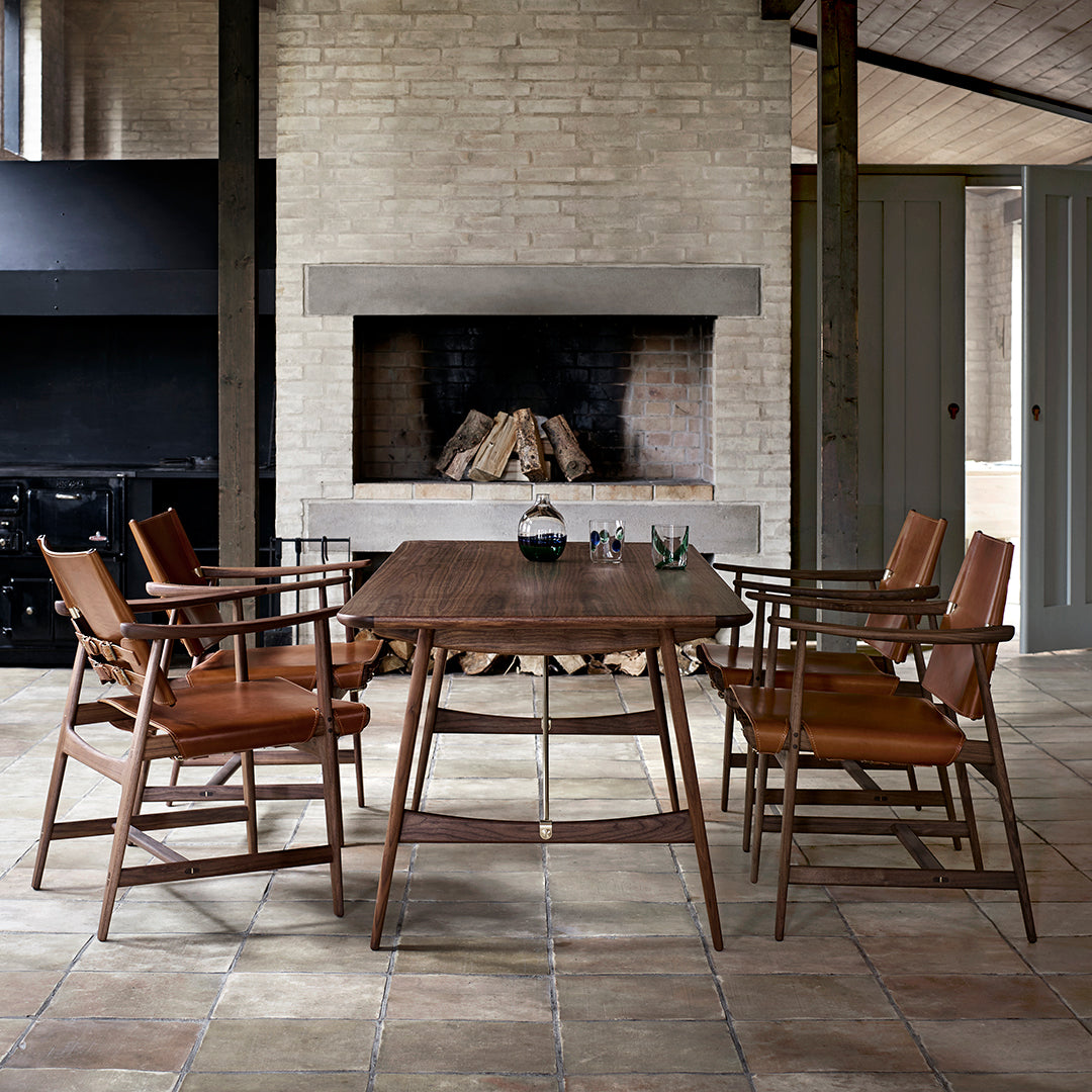 Wooden dining table with rich brown finish, complemented by tan leather seats and a textured stone floor.