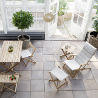 Natural wood furniture with white cushions, featuring a light, airy indoor space with stone tiles and greenery.