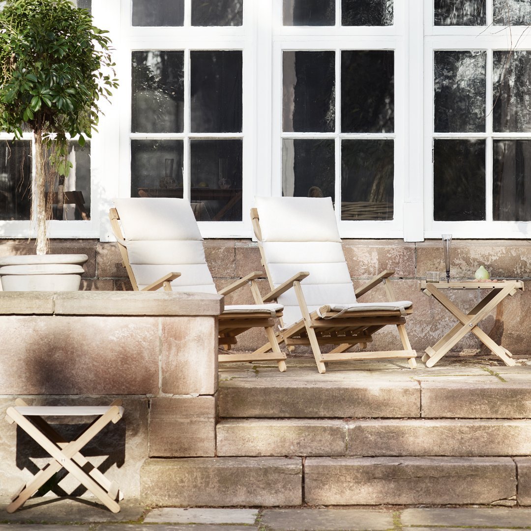 "Neutral-toned lounge chairs with subtle stripes, set against a warm, stone backdrop and white window panes."