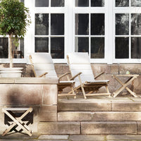 "Neutral-toned lounge chairs with subtle stripes, set against a warm, stone backdrop and white window panes."