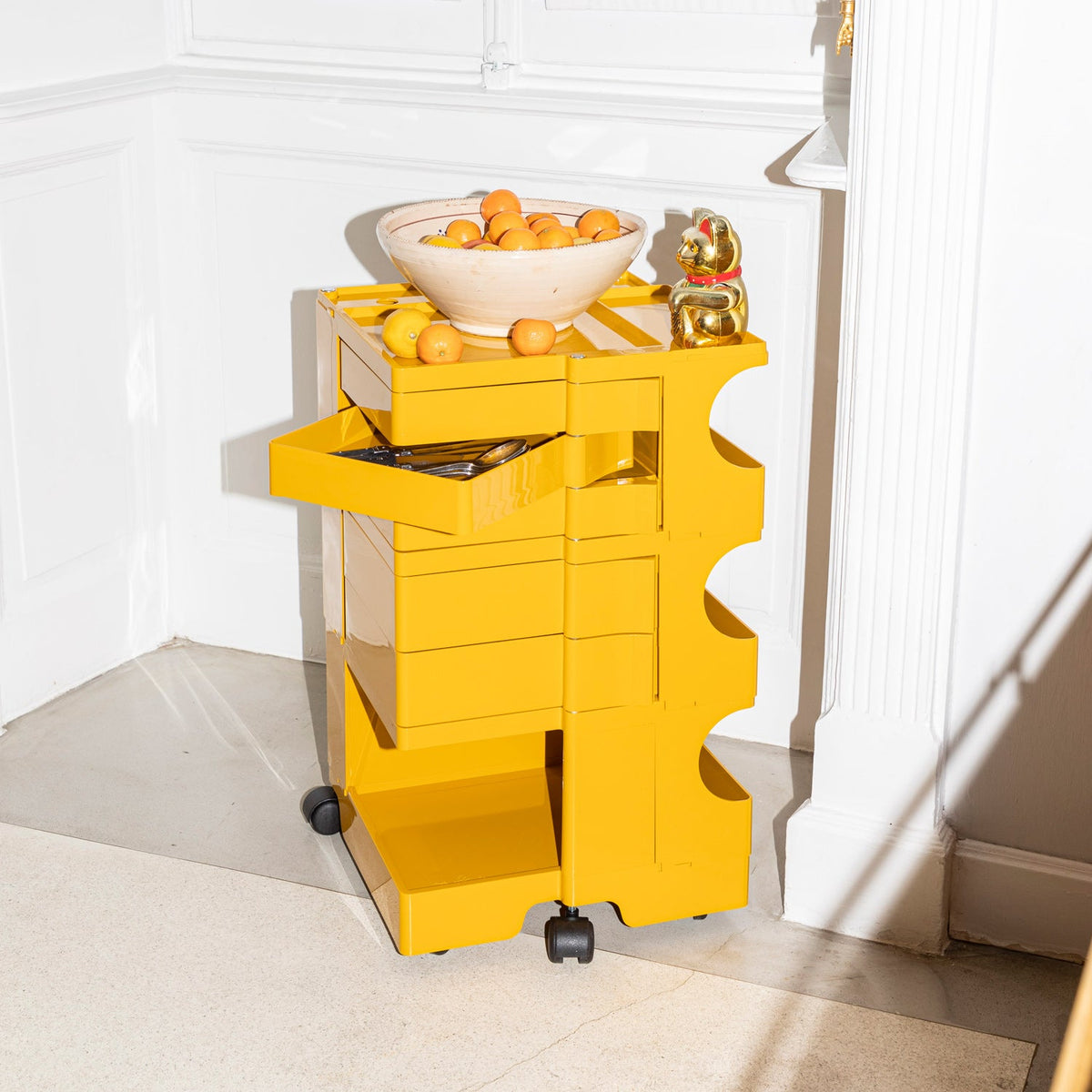 Bright yellow storage cart with glossy finish and modern design, featuring a bowl of oranges on top.