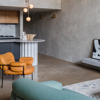 "Modern living room featuring a textured gray wall, orange accent chair, and light turquoise sofa with geometric patterns."