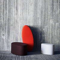 Colorful contemporary stools in red, white, and dark brown, featuring smooth, modern shapes against a textured gray background.