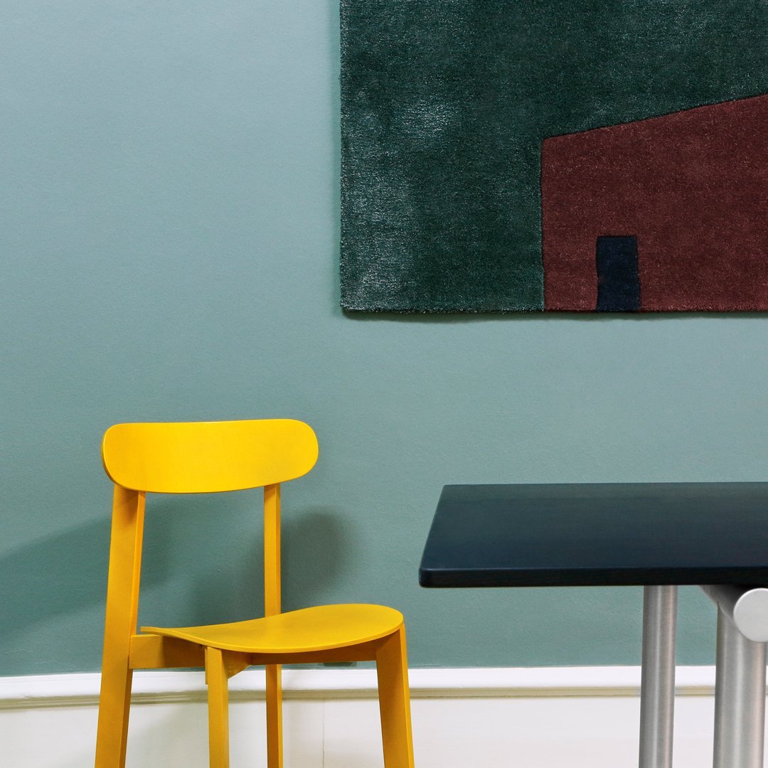Yellow chair beside a black table, with a green and brown patterned rug on a soft blue wall.