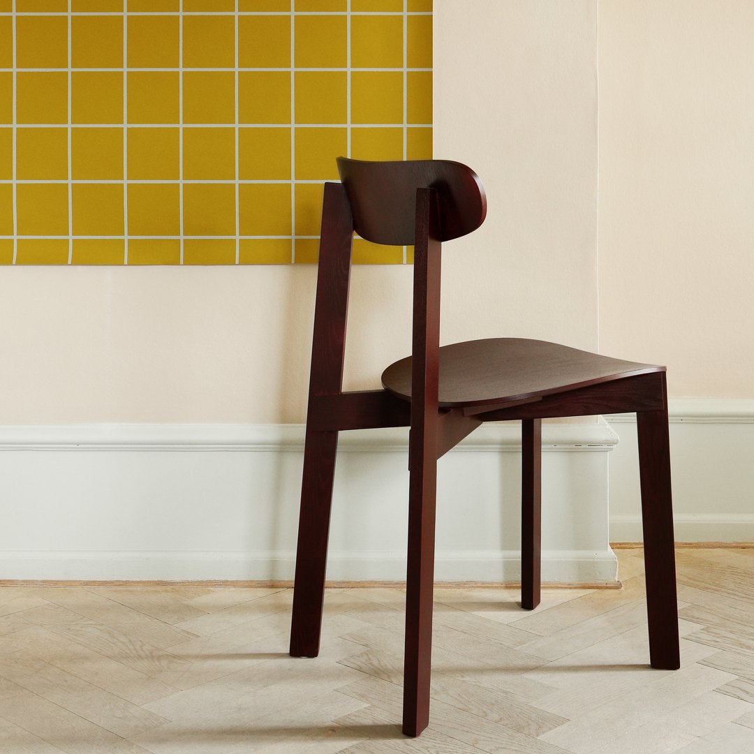 "Dark wood chair against a yellow grid-patterned wall, creating a modern contrast in colors and textures."