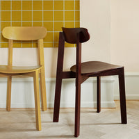 Two contemporary chairs: one golden yellow and one rich brown, set against a muted pastel wall and grid-patterned tile.