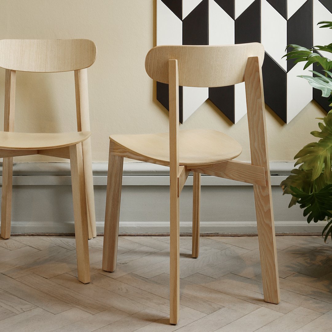 Light natural wood chair with a smooth finish, set against a geometric black and white wall pattern.