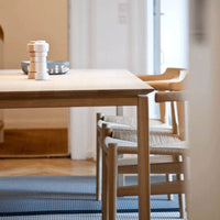 Natural wood table with beige chairs, accented by a blue plate and patterned woven rug in soft colors.