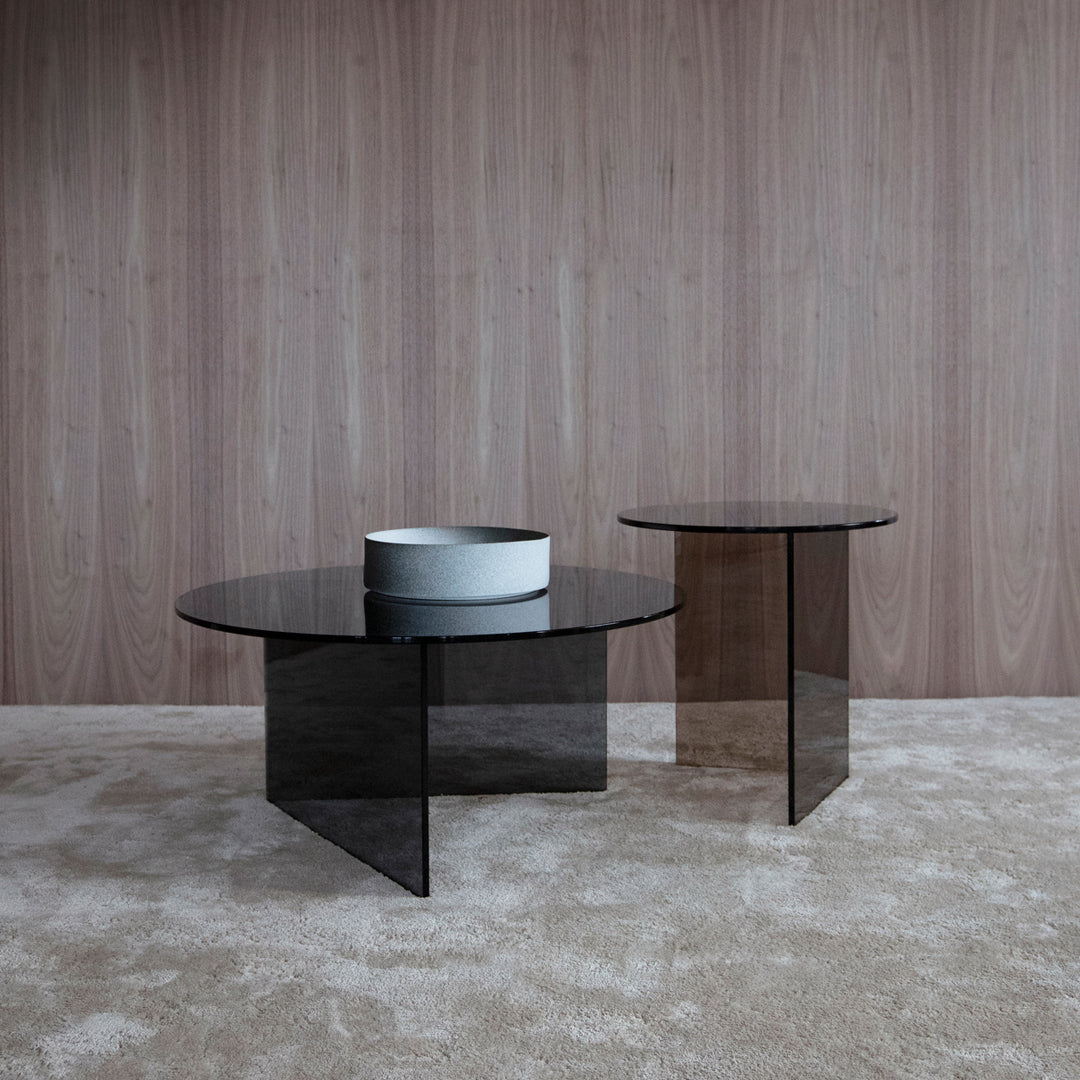 "Two stylish glass coffee tables with sleek black surfaces and geometric shapes against a textured wooden wall."