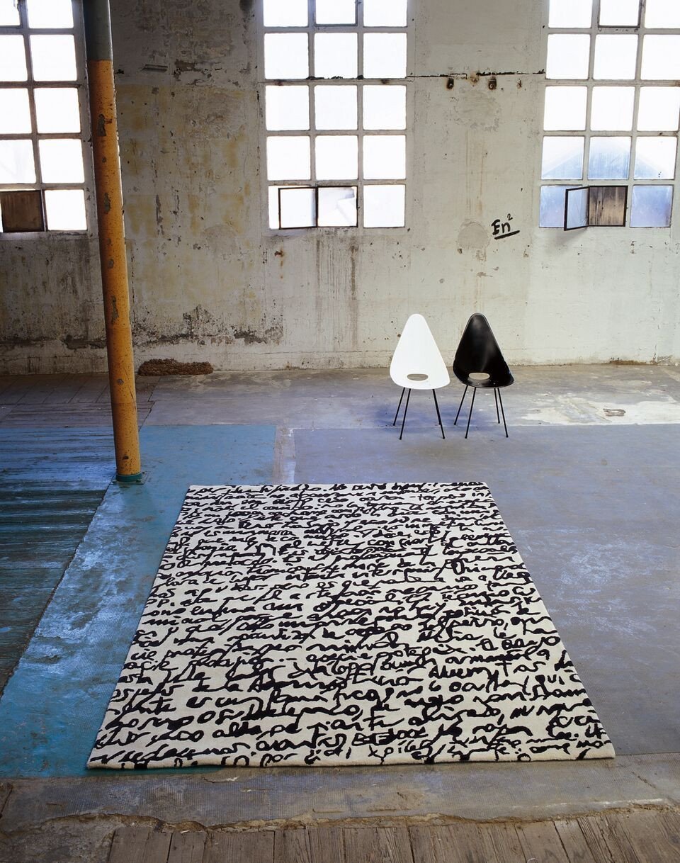 Black and white patterned rug with abstract script design, set against a rustic industrial background.