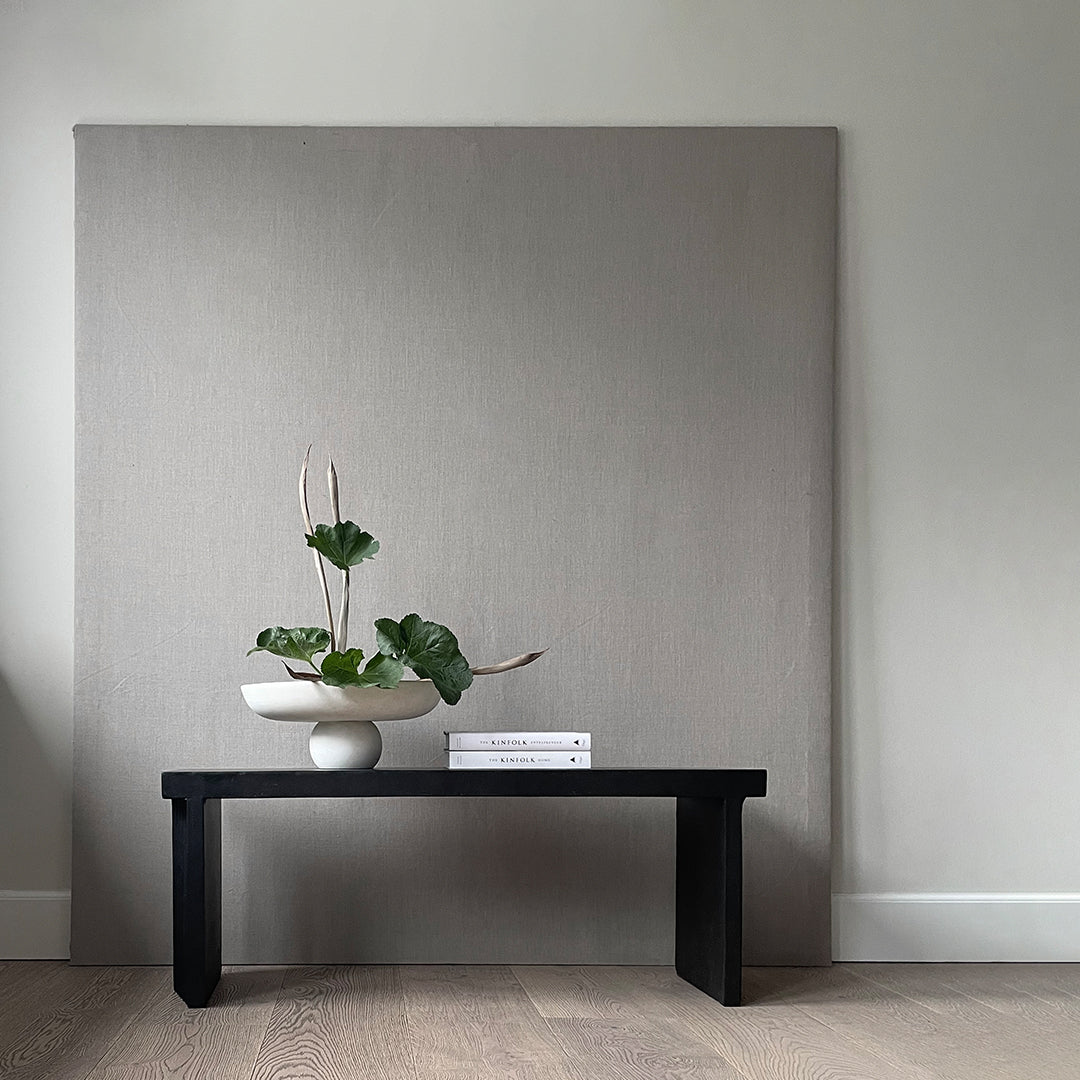 Gray textured backdrop with a black table, featuring a white vase and lush green plants for a modern aesthetic.