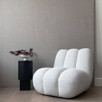 Textured white chair with plush, rounded shape and subtle linear pattern, alongside a sleek black side table.