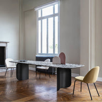 Modern dining table with a speckled white and gray top, complemented by black and pastel chairs in a light-filled room.