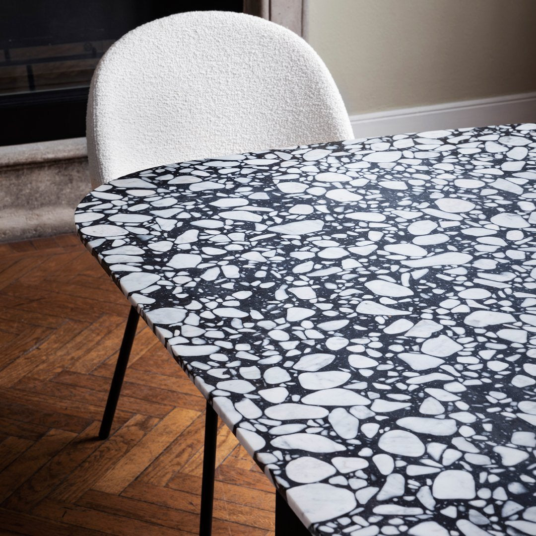 Black and white pebble-patterned tabletop with smooth finish, complemented by a cozy white chair.
