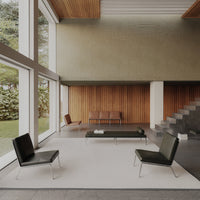 Modern living room featuring black chairs, a neutral-gray rug, and warm wood paneling. Natural light illuminates the space.