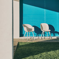 Modern white chairs on green grass with a vibrant blue backdrop, creating a fresh and stylish outdoor scene.