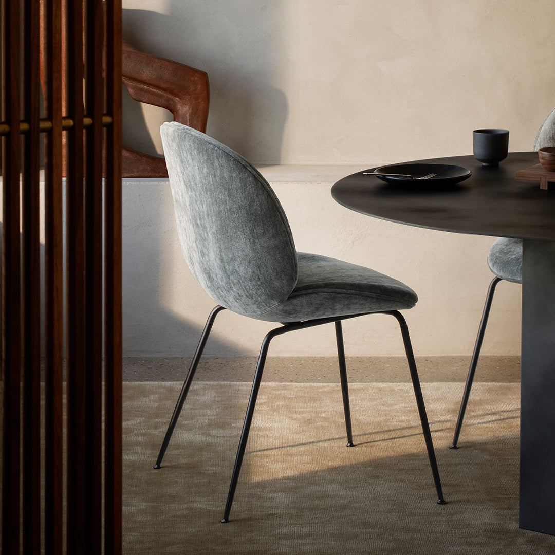Soft grey velvet dining chair with a sleek black metal frame, set against a warm beige background.
