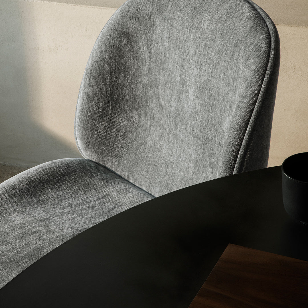 Soft gray upholstered chair with a smooth, rounded design beside a dark wooden table.